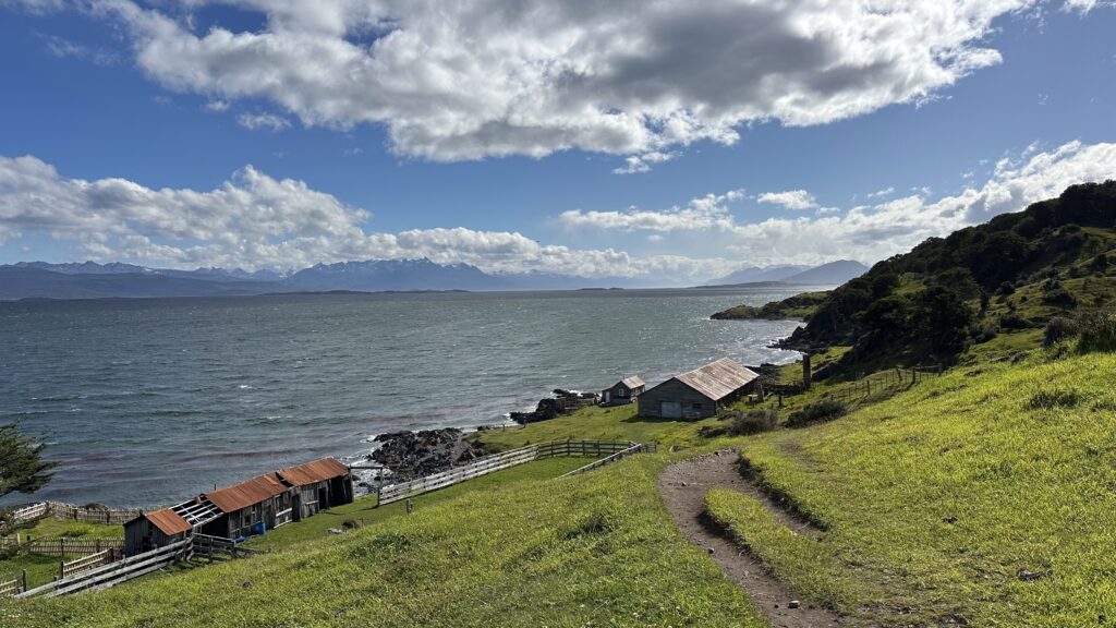 Canal Beagle Visto de um pasto bem verde e com uma casa de interior ao fundo