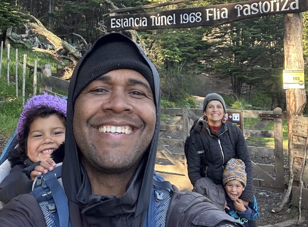 selfie de uma família de quatro pessoas: Pai, mão e um casal de filhos pequenos na entrada de uma trilha