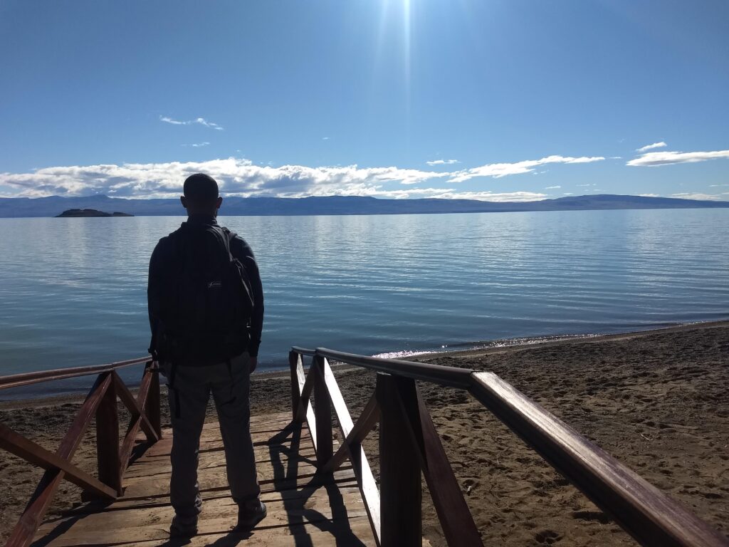homem de pé observando um grande lago à sua frente enquanto o sol brilha forte no céu