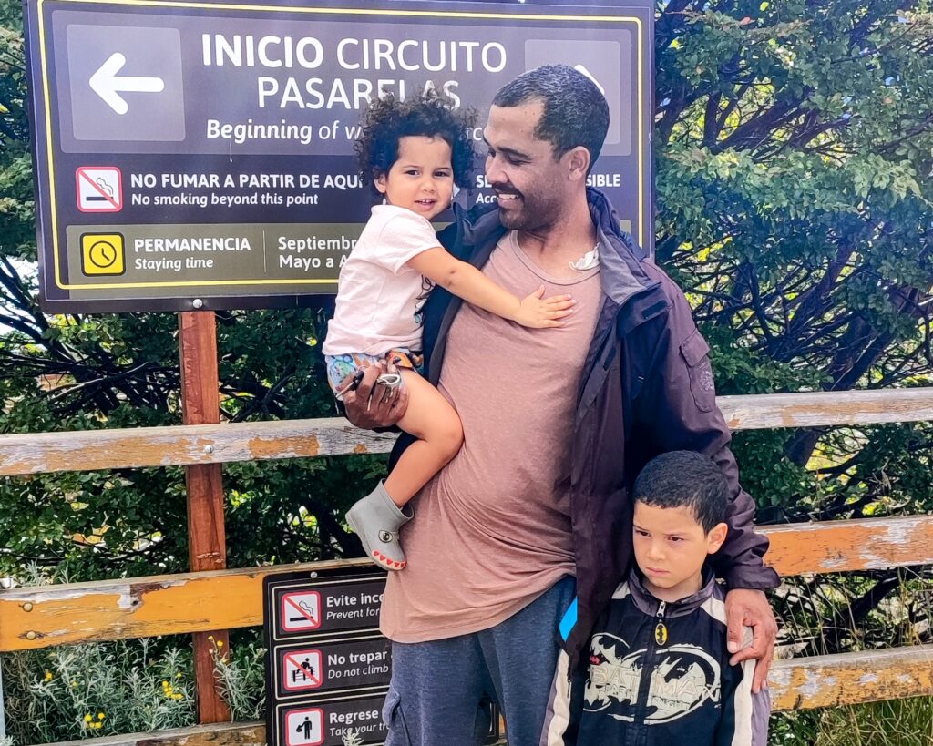 foto de um homem com uma criança no colo e abraçando outra cirança que está em pé ao seu lado