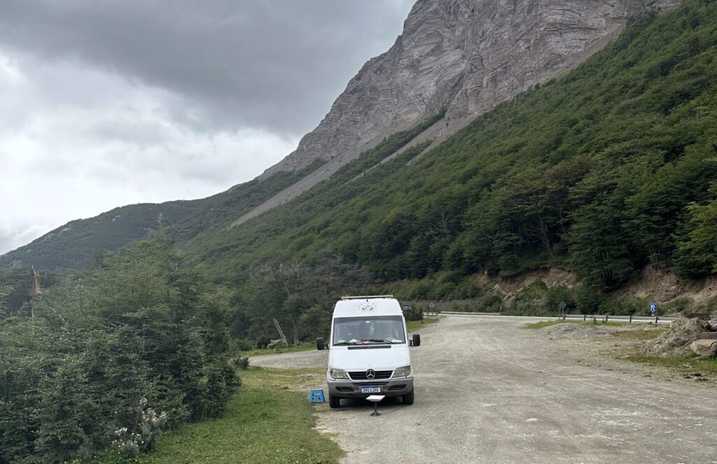 motorhome branco de frente parado num camping. De fundo uma montanha